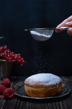 Berliner jelly filled doughnut with raspberry and redcurrant on wooden background.