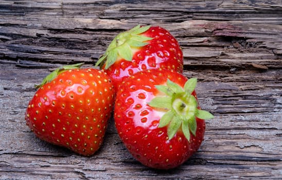 Three strawberries with strawberry leaf on old wooden background.