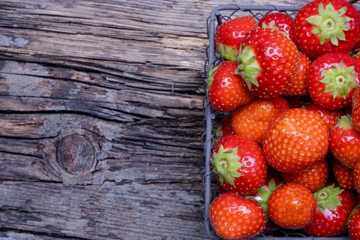 Strawberries with strawberry leaf in a metal basket, top view on old wooden background.