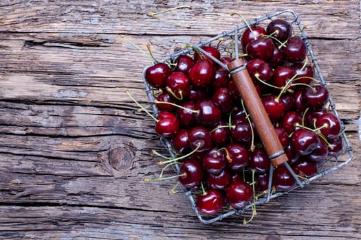 Fresh cherry fruit in a metal basket, top view on old wooden background.