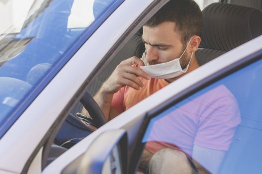 A young man, wearing a cloth face mask, checks the mobile phone inside the car, while he waits for someone before drive, in the province of Zaragoza, Spain.