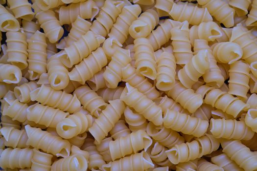 Uncooked rotini or fusilli pasta. Italian egg pasta as background.