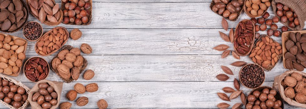 Panorama of various nuts, vegetarian food in wooden bowls, top view on old wooden background.