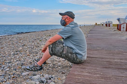 A man on the beach alone and wearing a protective mask looks at the baltic sea in the morning