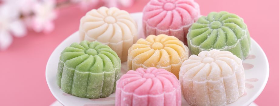 Colorful snow skin moon cake, sweet snowy mooncake, traditional savory dessert for Mid-Autumn Festival on pastel pale pink background, close up, lifestyle.