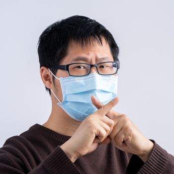 Portrait of young Asian man, saying no to coronavirus infection with wearing medical surgical blue face mask isolated on white background, close up, closeup.