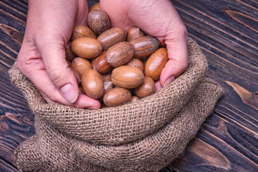 Close up woman hand holds pecan nut on a wooden background.