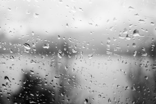 Raindrops on a window, illustrating gray and rainy weather during the day. Black and white grayscale.