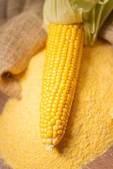 Ripe young sweet corn cob,on stack cornmeal on wooden background,close up.Gluten free food concept