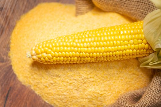 Ripe young sweet corn cob,on stack cornmeal on wooden background,copy space.Gluten free food concept