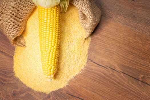 Ripe young sweet corn cob,on stack cornmeal on wooden background,copy space.Gluten free food concept