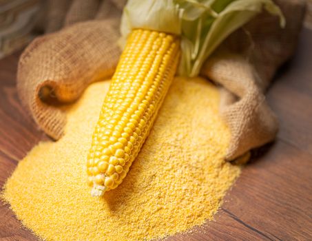 Ripe young sweet corn cob,on stack cornmeal on wooden background,copy space.Gluten free food concept