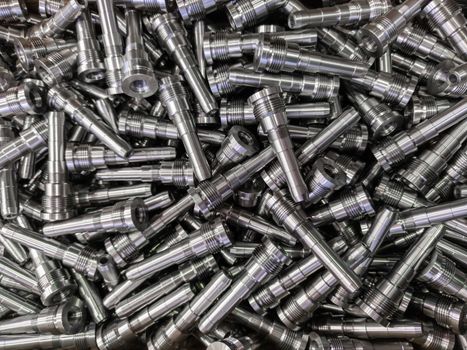 Full frame background of pile of shiny long steel parts, clean steel rods after fine cnc turning - laying chaotically with selective focus and blur.