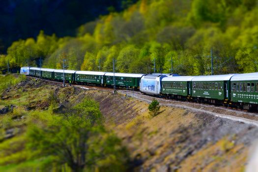 Flam, Norway, May 2015: train carriages of the Flamsbana (Flam Line) running through a green valley. Flam railway is a railway line between Myrdal and Flåm in Aurland, Norway.