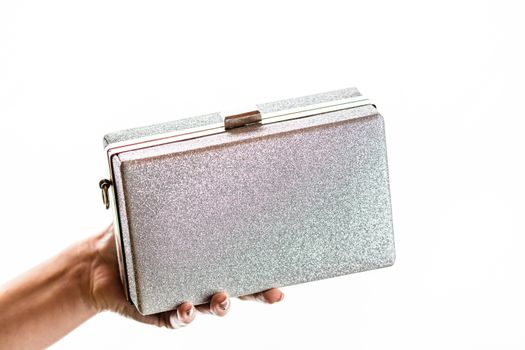 Woman hand holding glittery silver clutch bag isolated on white background with copy space.