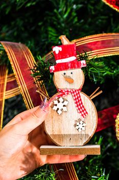 Hands holding Christmas snowman figurine in front of the Christmas tree. Decorating the fir tree isolated