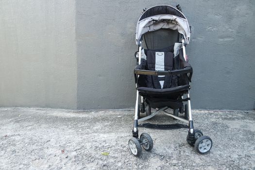 Black color baby stroller with head covering. Stroller is with concrete background