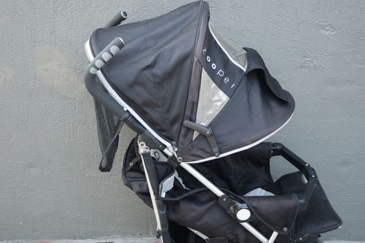Black color baby stroller with head covering. Stroller is with concrete background