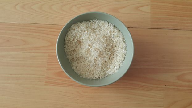 Top closeup view of heap of rice in a ceramic bowl placed over wooden floor.