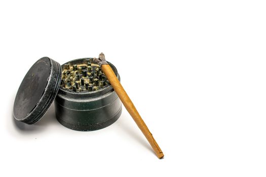 A Lit Cannabis Cigar Leaning on a Black Grinder With the Lid Leaning on the Side