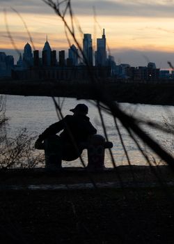 A Man Leaning On Two Poles at Graffiti Pier With the Philadelphia Skyline Behind Him