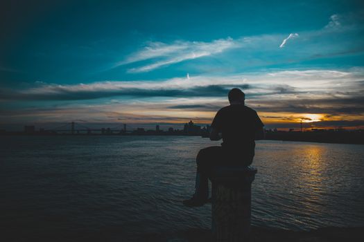 A Silhouette of a Man Sittnig on a Pole With a Dramatic Orange and Blue Sunset Behind Him