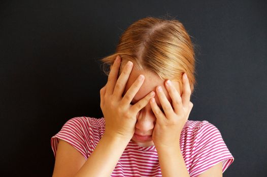 teenage girl holding a sick head with her hands, portrait on a black background.