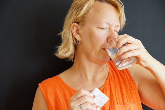 sick woman drinks pills with water, portrait on black background.