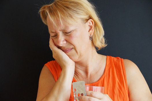 unhappy woman holding her hand for a bad tooth, in the other hand pills and water.