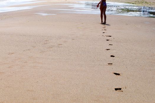 feet of a young girl walk barefoot on a wet beach, leaving footprints in the sand.