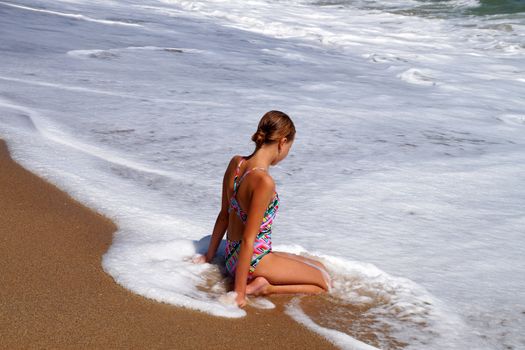 teenage girl sitting on a sandy beach in sea white foam.