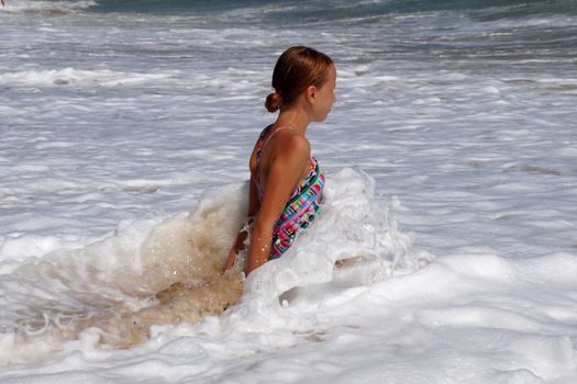 teenage girl sitting on a sandy beach in sea white foam.
