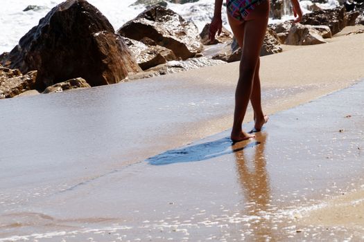 teenage girl walking alone along the empty seashore on the sunny day, rear view