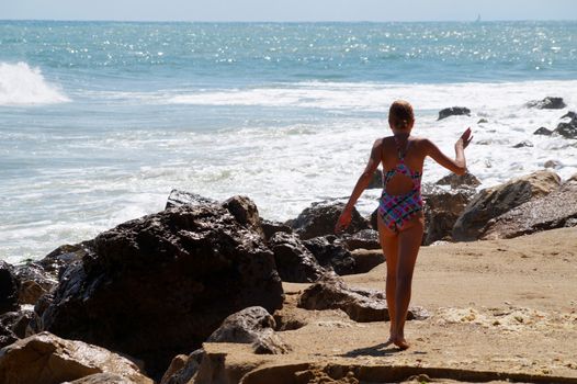 teenage girl walking alone along the empty seashore on the sunny day, rear view