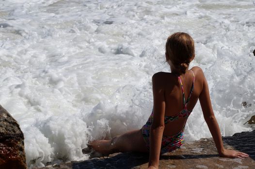 teenage girl sitting on a sandy beach in sea white foam.