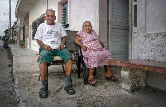 Progreso, Mexico - October 14, 2007: Old couple of Progreso residents sitting on their porch on a hot evening with tired expression in their face.