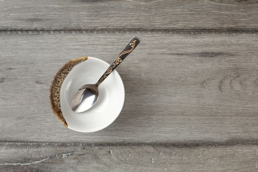 Table top view on small empty porcelain bowl with silver decorated spoon, placed on gray wood desk.