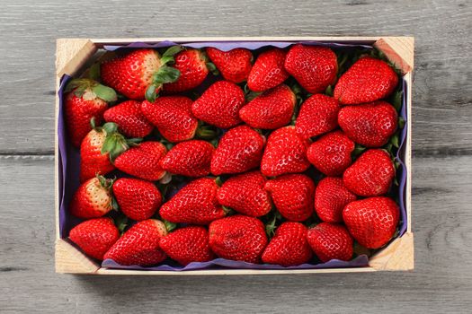 Table top view on small box of strawberries from supermarket placed on gray wood desk.