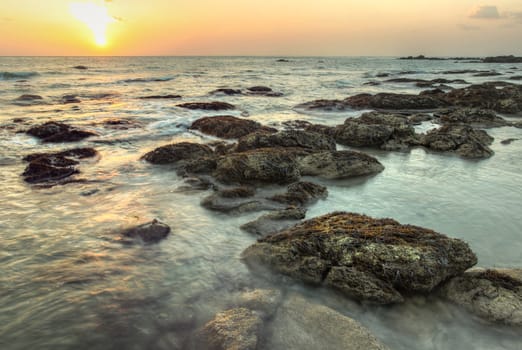 Sunset during low tide on Koh Lanta, Thailand. Algae covered rocks in shallow sea.