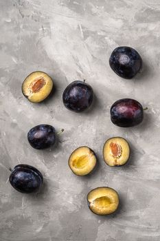 Fresh ripe plum fruits whole and sliced with water drops on stone concrete background, top view