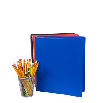 Photograph of colorful pencils in pencil holder and stack of brightly colored notebooks with copy space isolated on a white background. 