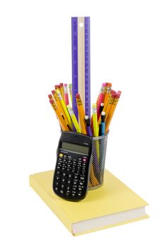 Vertical photograph of brightly colored pencils  and calculator on a yellow book. Isolated on white background.