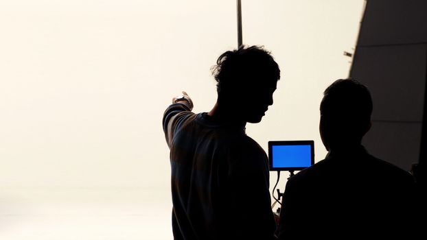 Movie director and photographer are talking or consulting to making studio set before shooting video and silhouette background lighting.