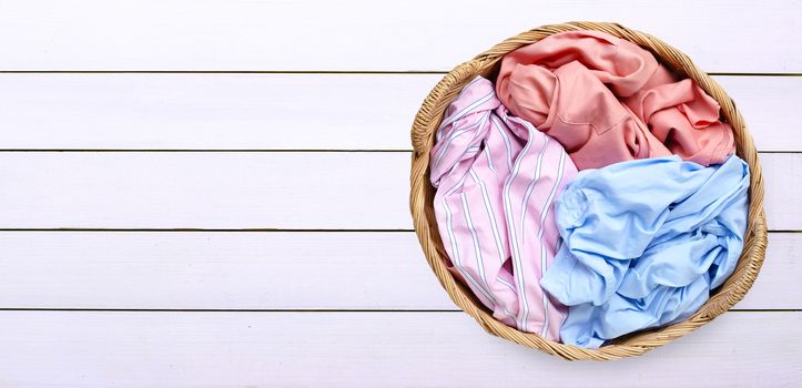 Colorful clothes in laundry basket on white wooden background. Copy space