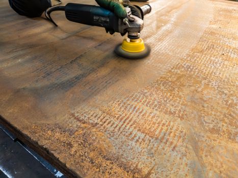 a process of manual cleaning of rusted sheet metal with steel brush on angle grinder.