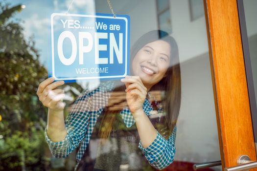 Closeup hand of Asian young woman setting open sign at the shop glasses for welcome the customer in to the coffee shop, small business owner and startup, installing open and close label concept
