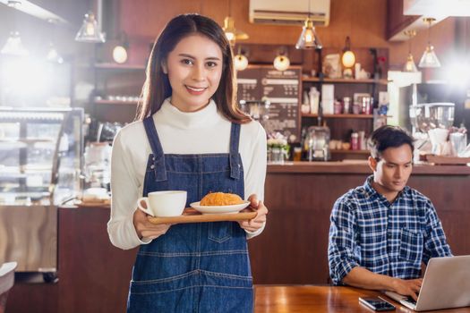 Asian Barista of Small business owner serving a cup of coffee and Croissants bakery to young customer at the table in coffee shop,Small business owner and startup in coffee shop and restaurant concept