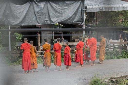 Monks in orange robes collect food donations in the morning. Monks on the streets in the city of Pakse, Laos.