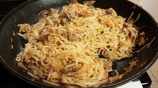 asian noodles and pork in frying pan or skillet on stove
