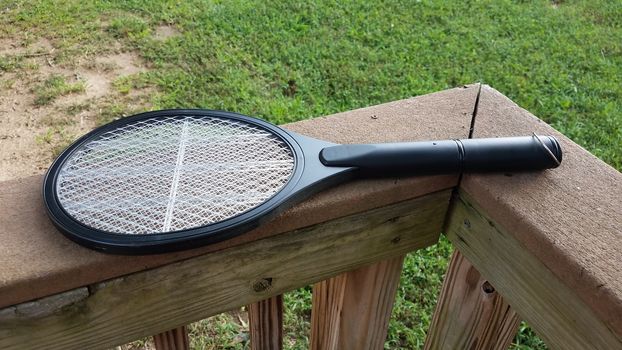 electronic metal tennis racket insect killer on wood deck railing